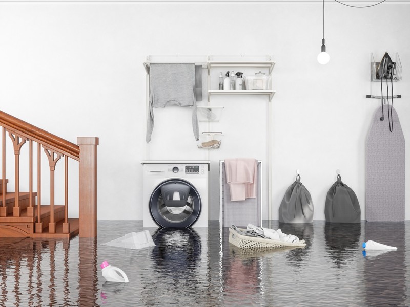 Flooded laundry room with washing machine, stairs, and cleaning supplies floating in standing water